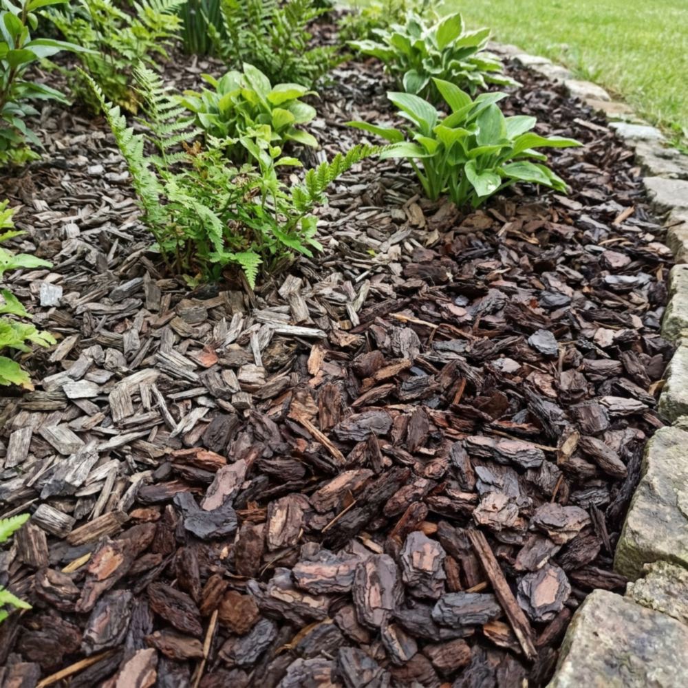 Border met verse donkere boomschors naast oudere vergrijsde schors rond groene tuinplanten