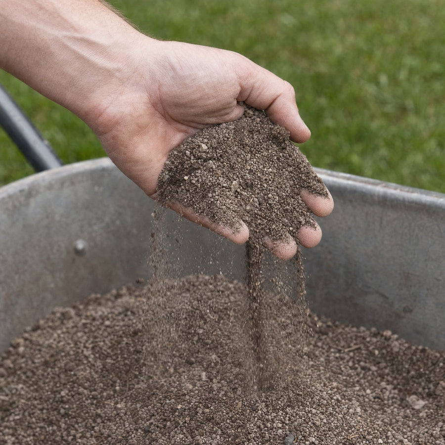 Hand met fijne topdressing van lava, zand en turf boven een kruiwagen