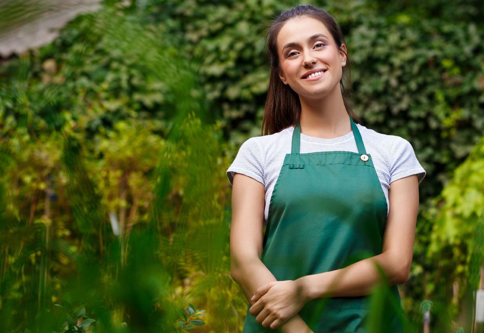 Lachende vrouw met groene tuinschort tussen de planten